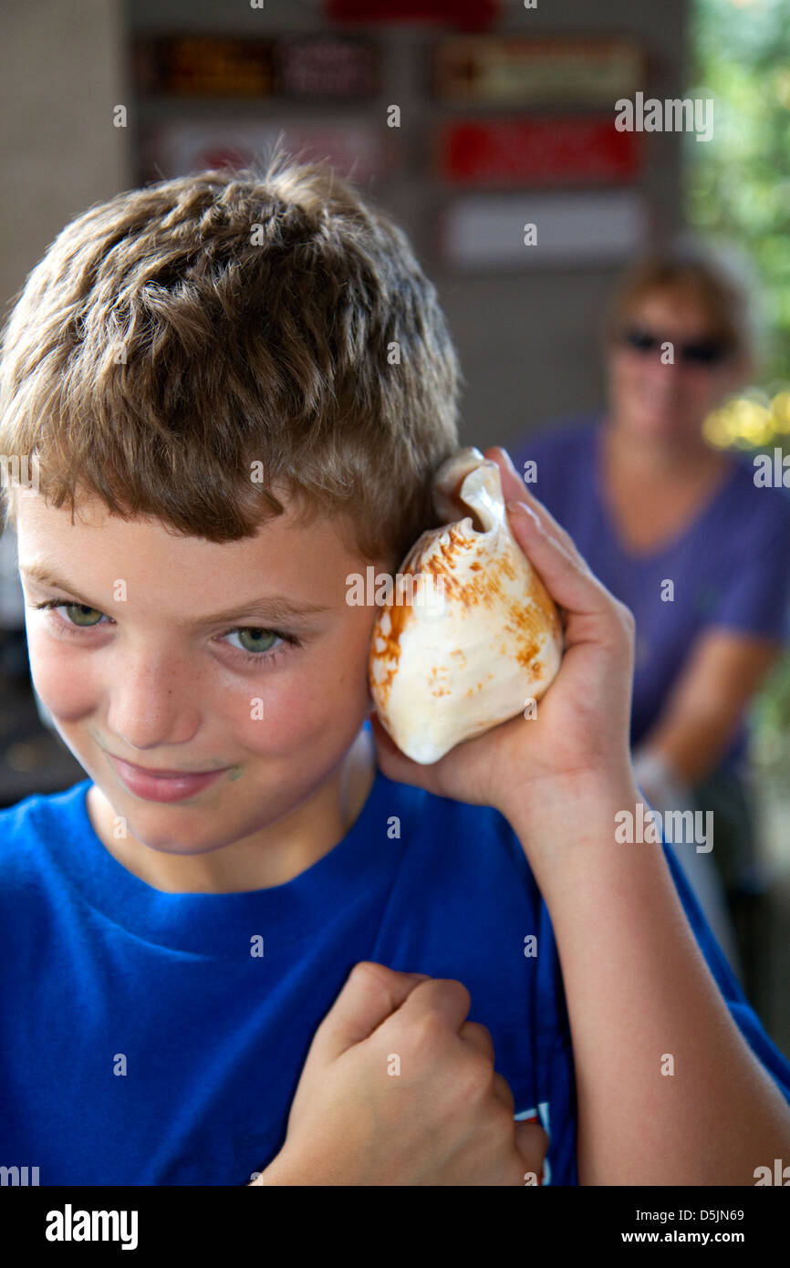 Eight year old boy listening to the ocean in a sea shell at John's Pass