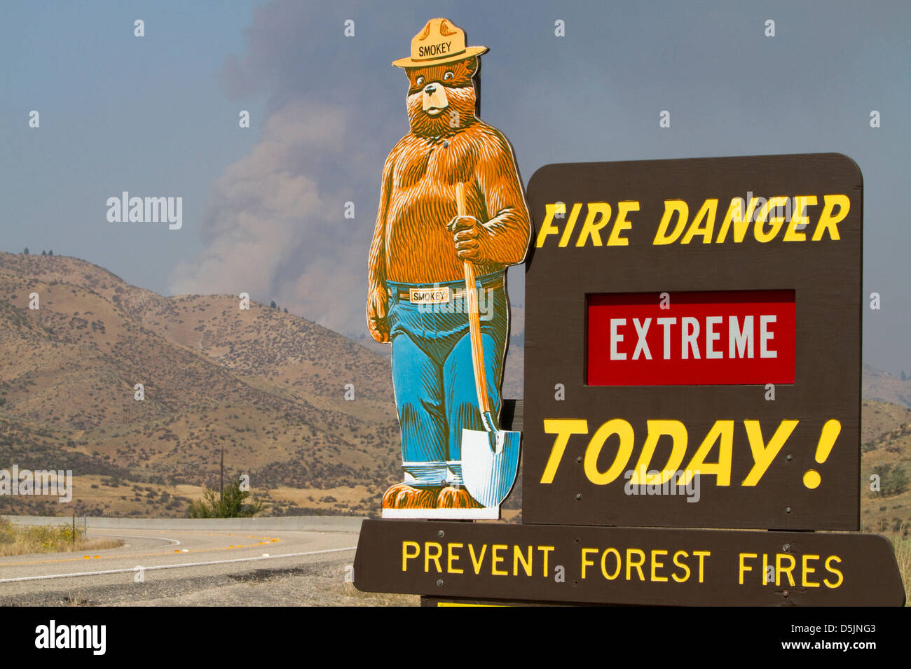 Smokey Bear extreme fire danger sign with a plume of smoke from a forest fire in the back ground in Boise County, Idaho, USA. Stock Photo