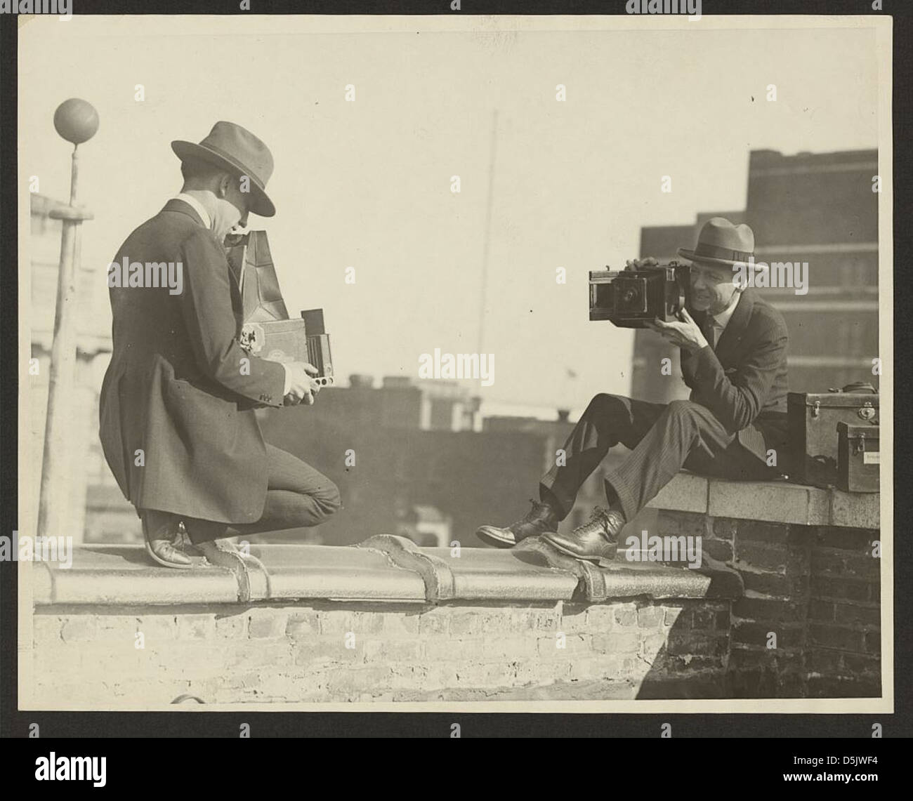 [Two photographers taking each others' picture with hand-held cameras while perched on a roof] (LOC) Stock Photo