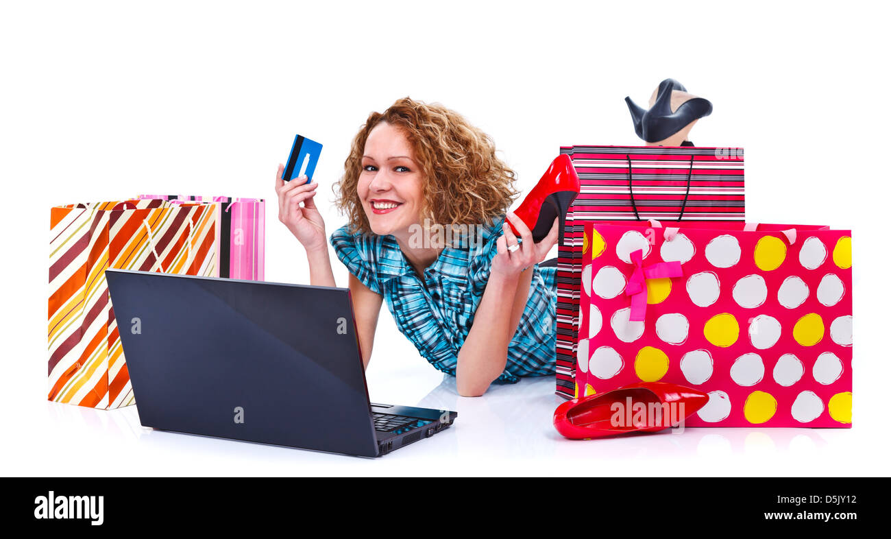 Happy young shopping woman with laptop, shopping bags holding a credit card and a red shoe - isolated Stock Photo