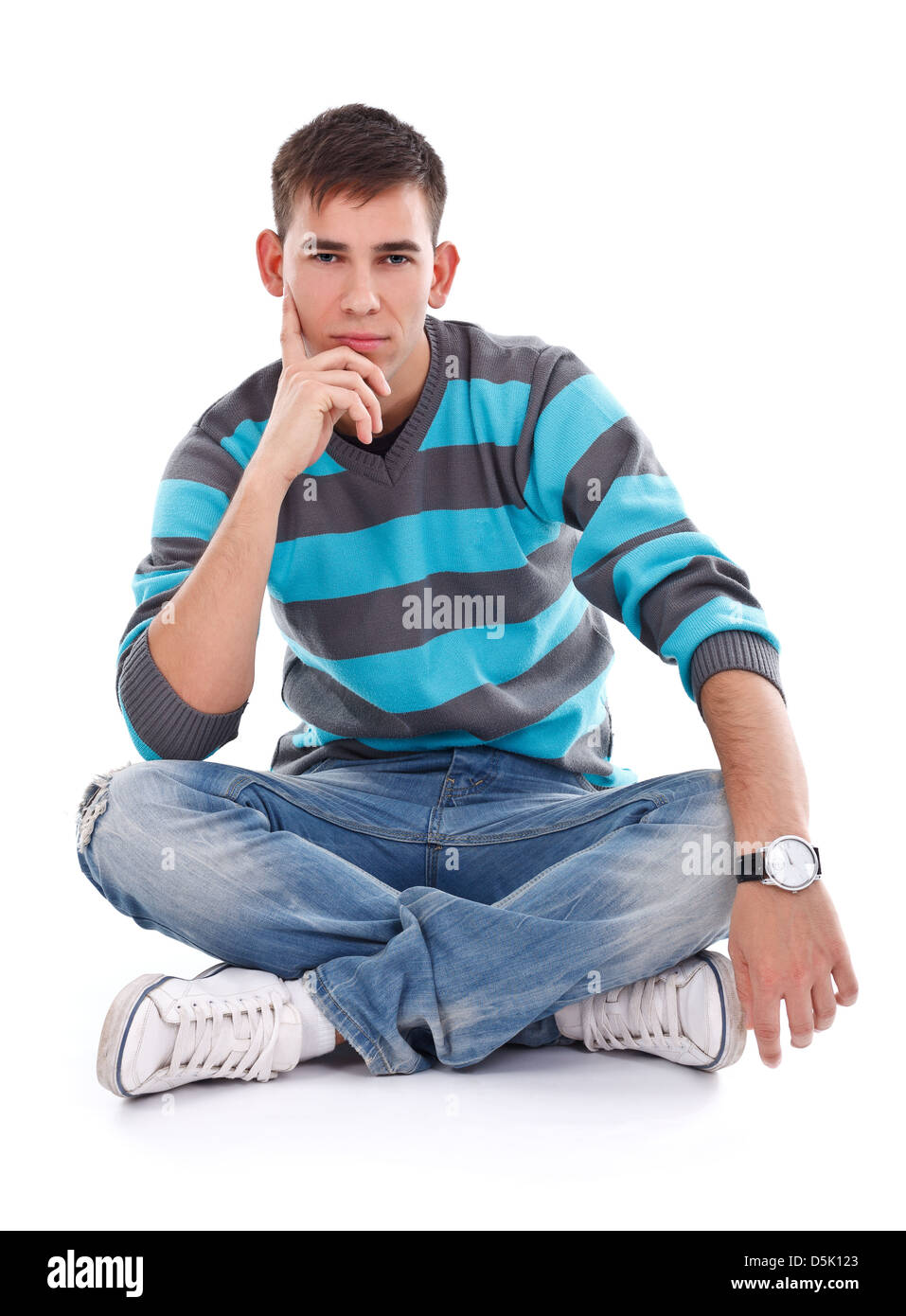 Portrait of a young man in jeans sitting on the floor with crossed legs isolated on white background Stock Photo