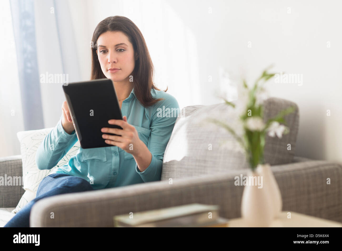 Woman using digital tablet while sitting on sofa Stock Photo - Alamy