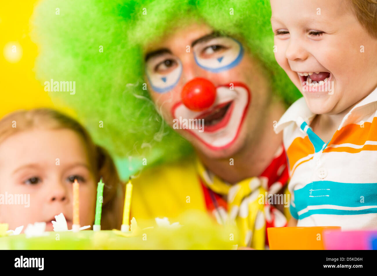 kids with clown celebrating birthday party and blowing candles on cake Stock Photo