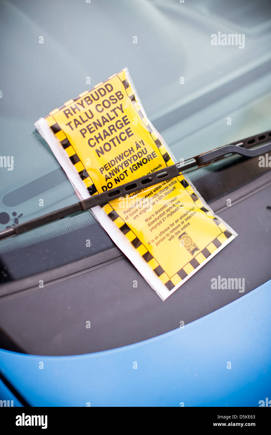 A bilingual penalty charge notice parking ticket in both English and Welsh beneath a car windscreen wiper. Stock Photo