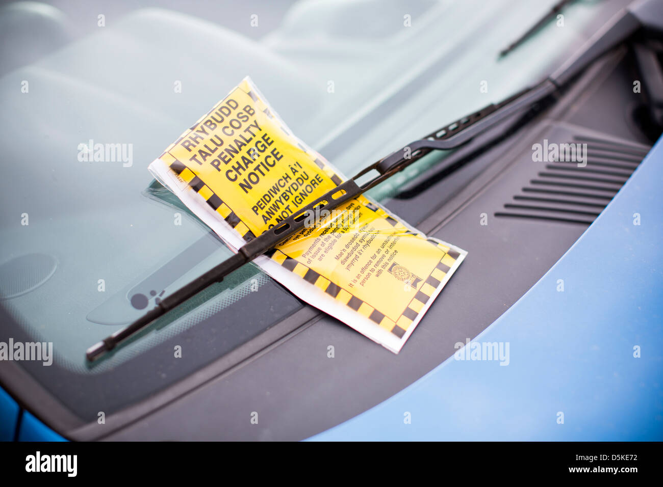 A bilingual penalty charge notice parking ticket in both English and Welsh beneath a car windscreen wiper. Stock Photo
