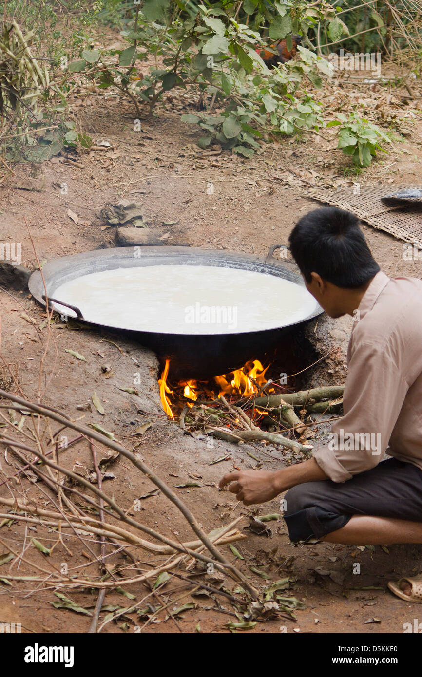 A man tending an open fire and brewing a traditional rice whisky  in a large flat iron pan. Stock Photo