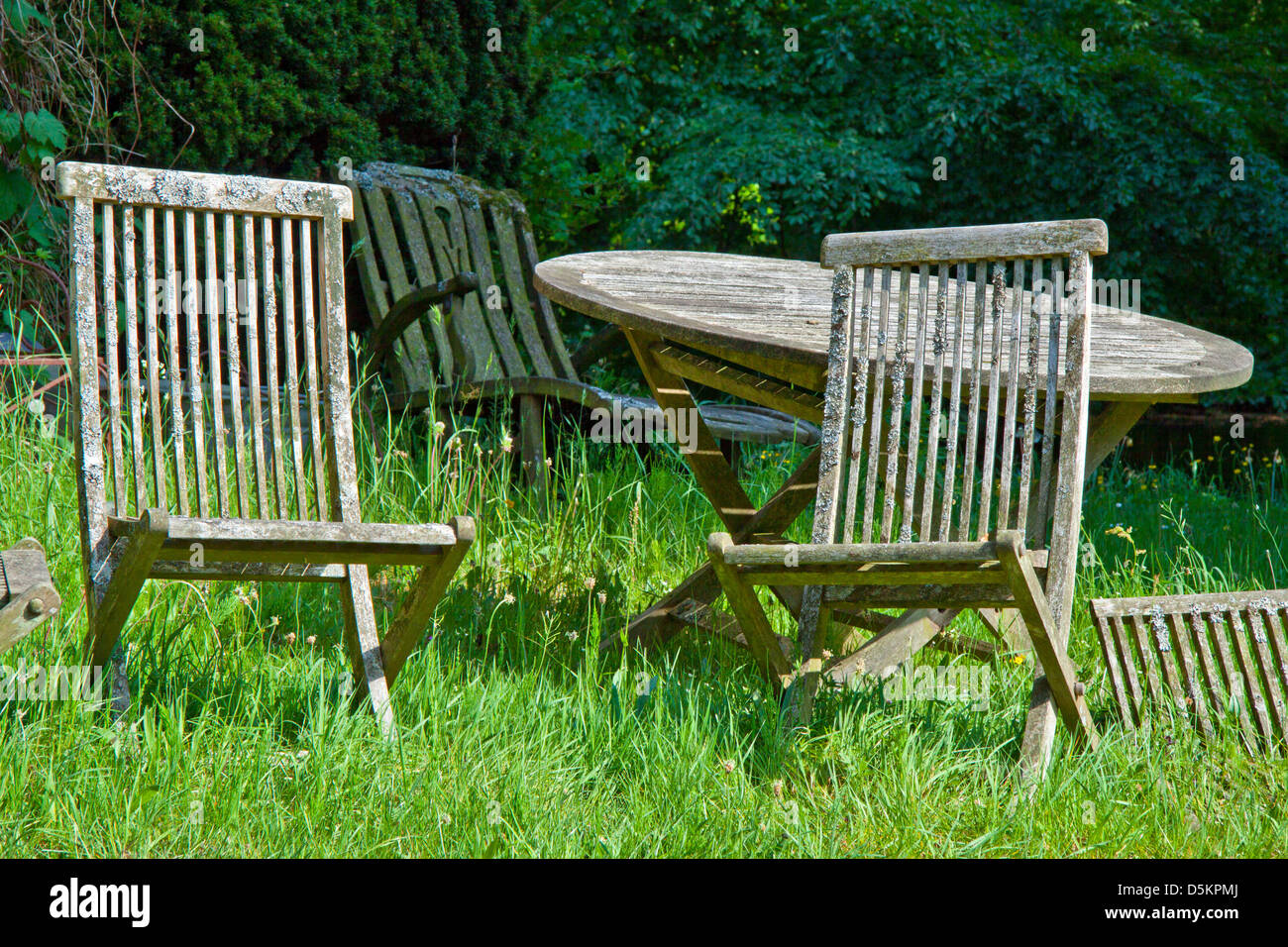 Deserted garden with old wooden table and chairs on grass Stock Photo