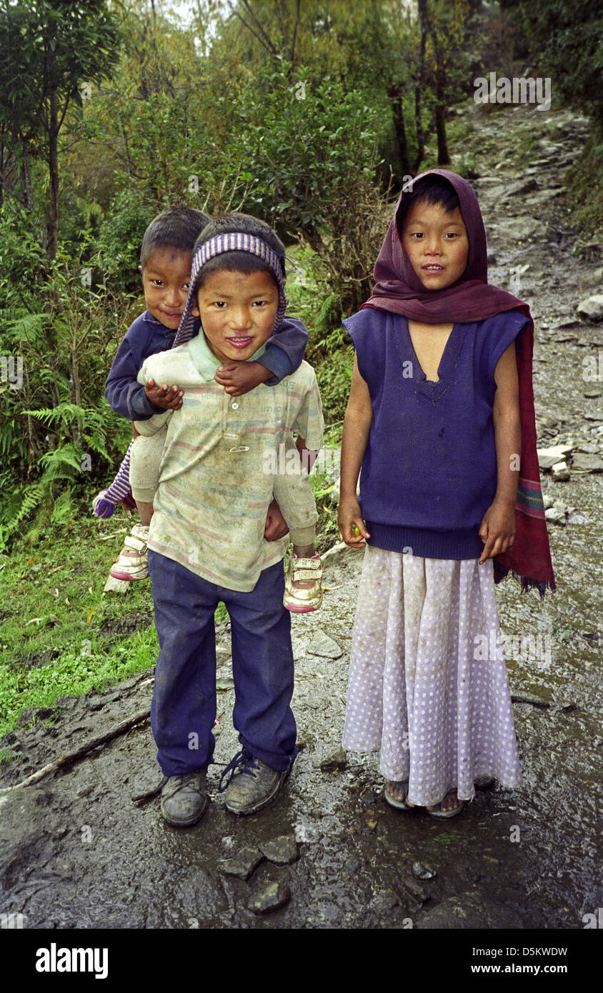 Three cute Nepalese children on Annapurna circuit track near Sikha Nepal Himalayas One boy carries another piggy back Stock Photo