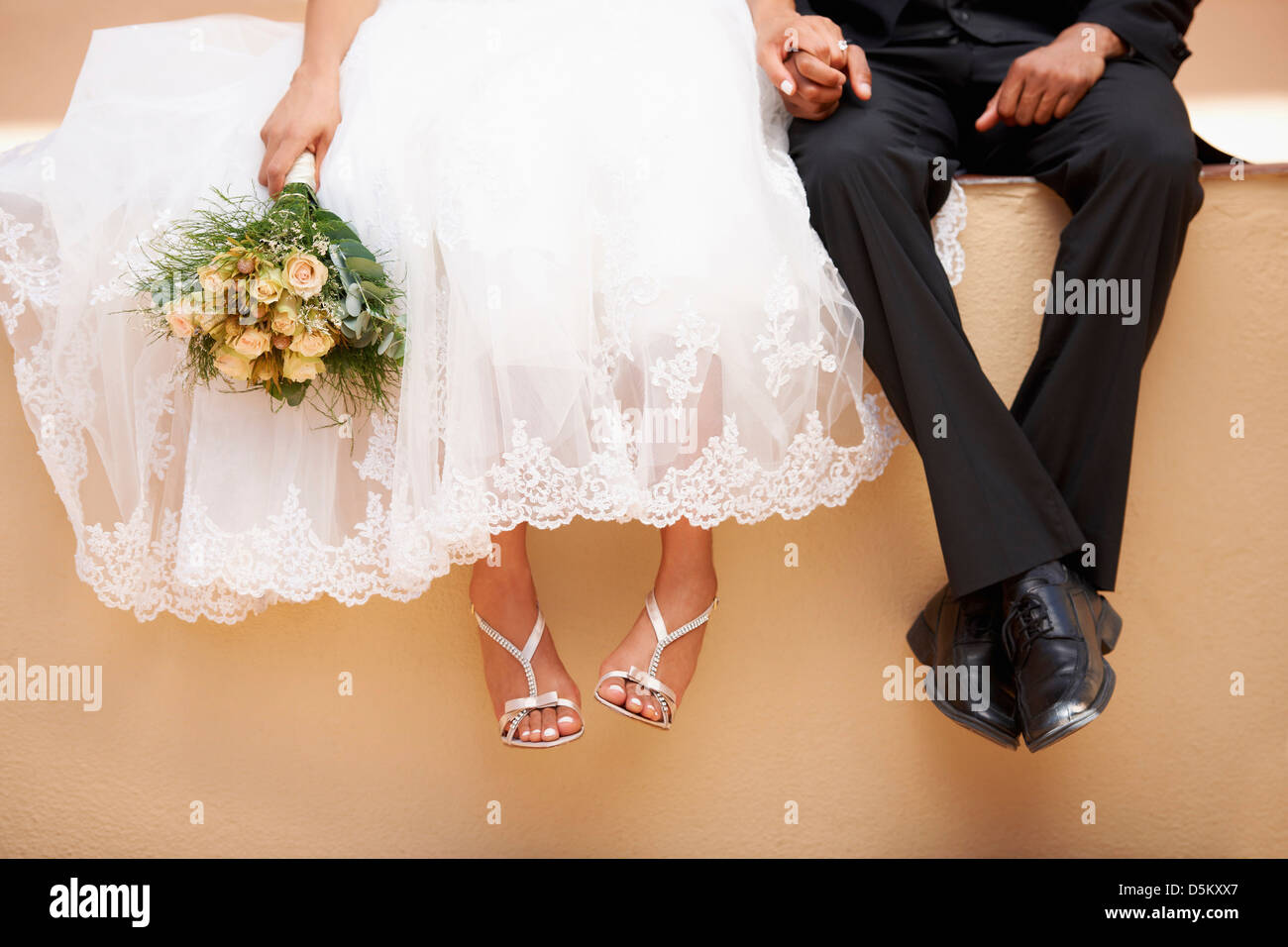 Bride and groom sitting on wall Stock Photo - Alamy