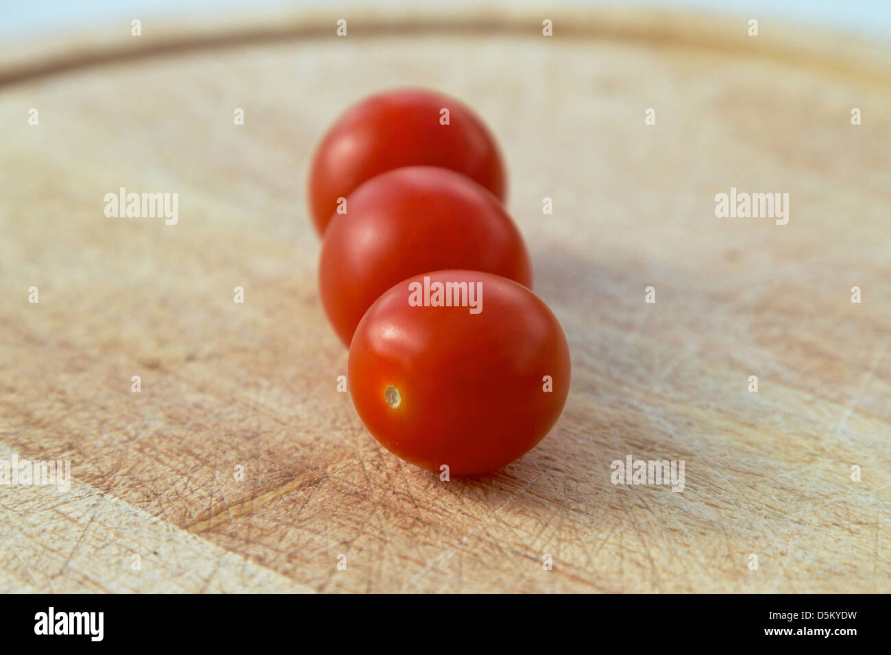 three cherry tomatoes on a chopping board Stock Photo - Alamy