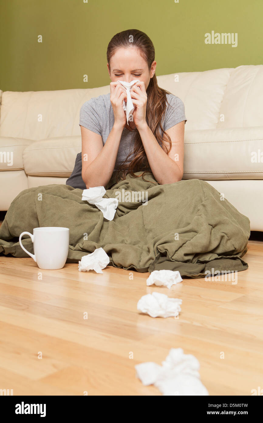 Woman in living room blowing her nose Stock Photo