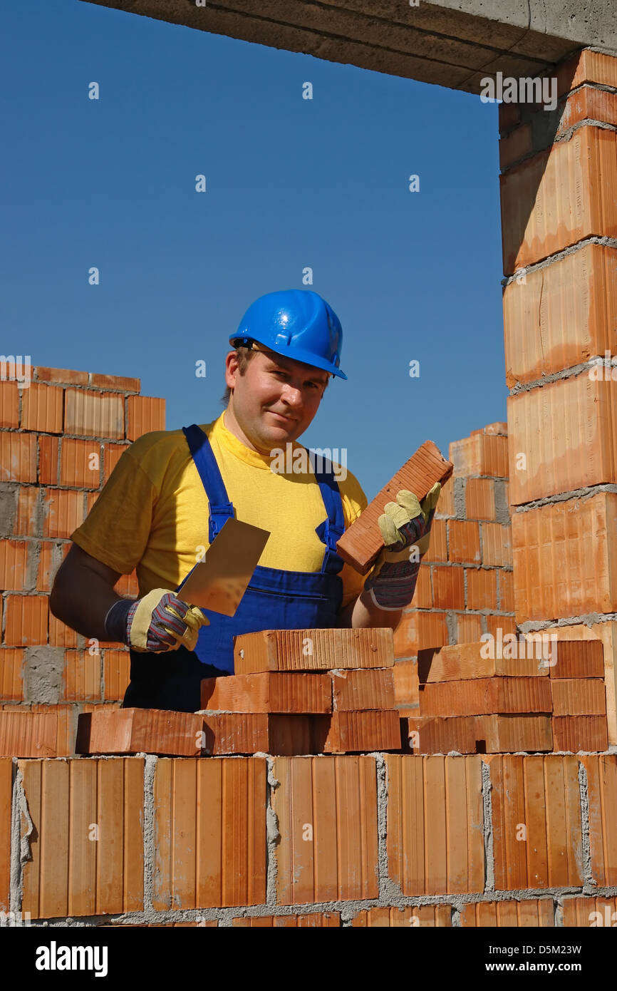 Mason in blue helmet building house wall in bricks Stock Photo