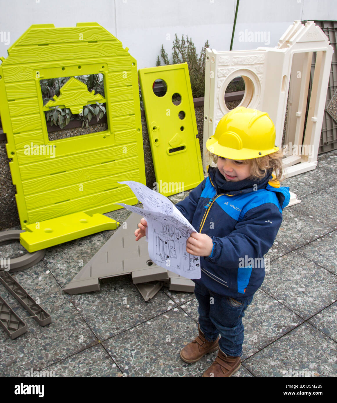 3 years old boy is playing at home. Assembling at toy house, wears a toy hard hat. Looks like an architect. Stock Photo