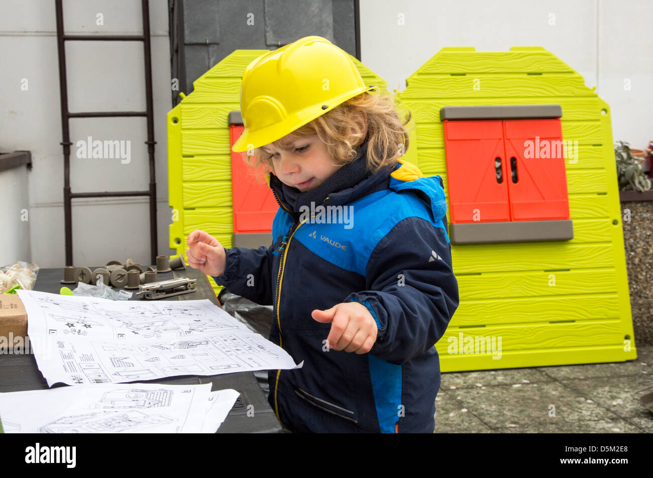 3 years old boy is playing at home. Assembling at toy house, wears a toy hard hat. Looks like an architect. Stock Photo