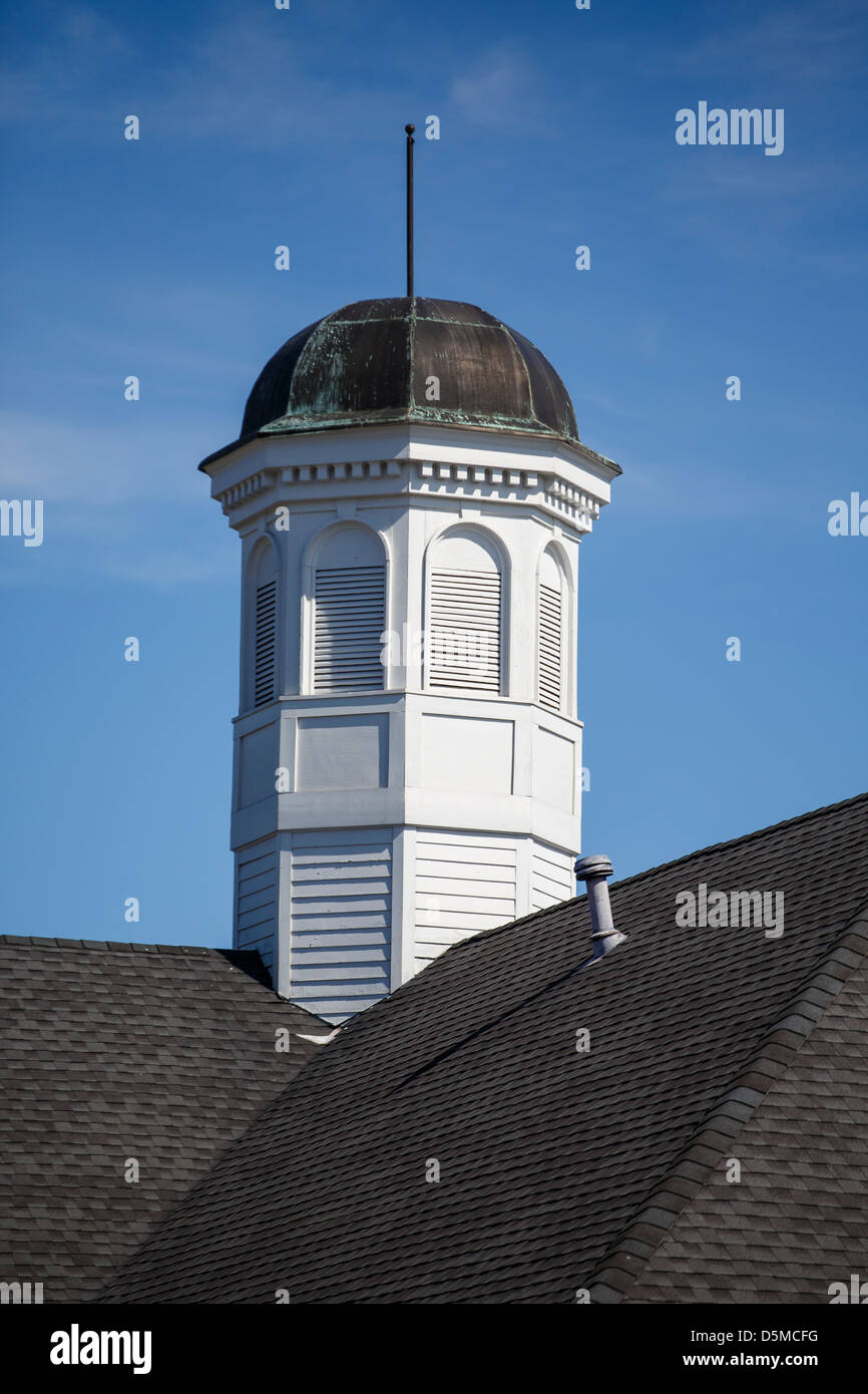 A white wood cupola on a grey shingled roof with tarnished copper top under clear blue skies Stock Photo