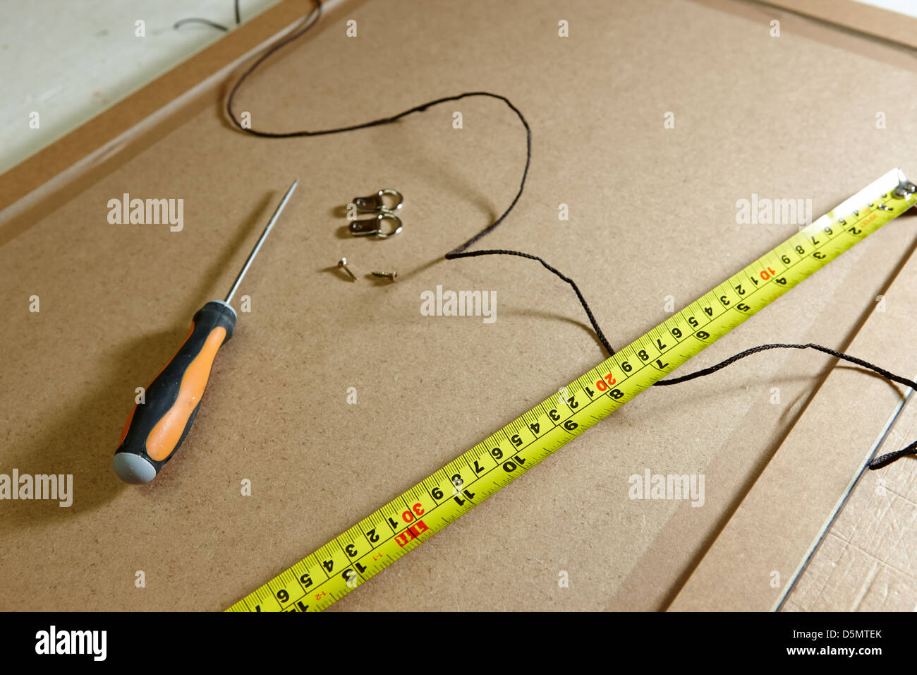 measuring tape screwdriver hanging strings and fixings on the back of a picture frame in a framing workshop Stock Photo