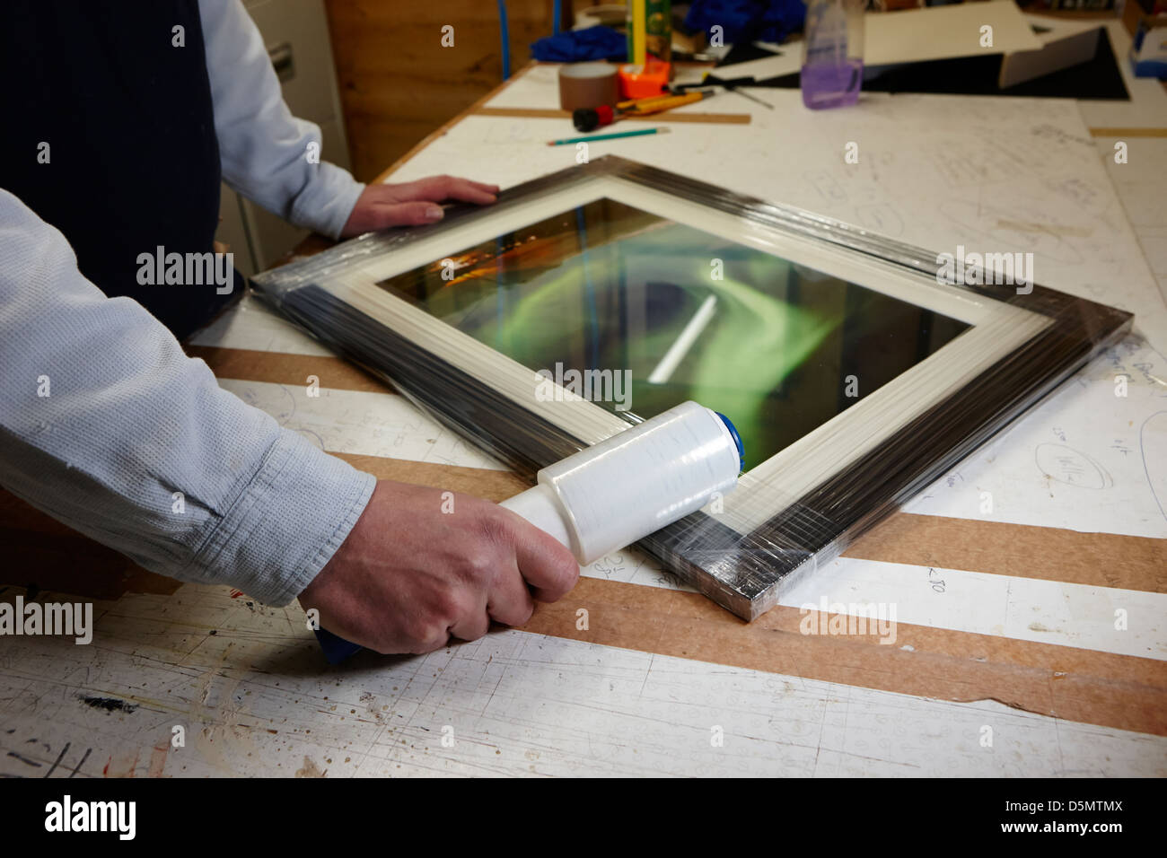 framer plastic wrapping edges of finished picture frame in a framing