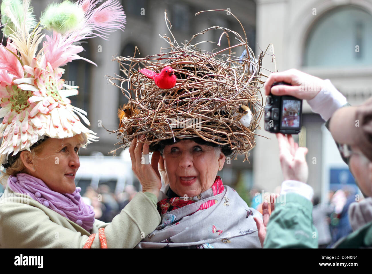 One woman adjusts another's hat, which resembles a bird's nest, as a man  takes a picture, at New York's City's Easter Parade Stock Photo