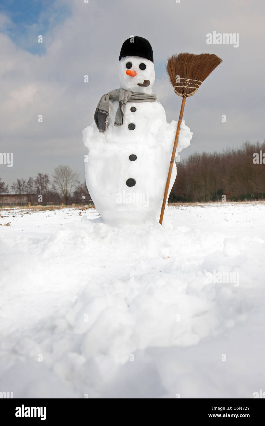 Decorated happy snowman with carrot nose, hat, pipe, scarf and broom in the snow in winter Stock Photo