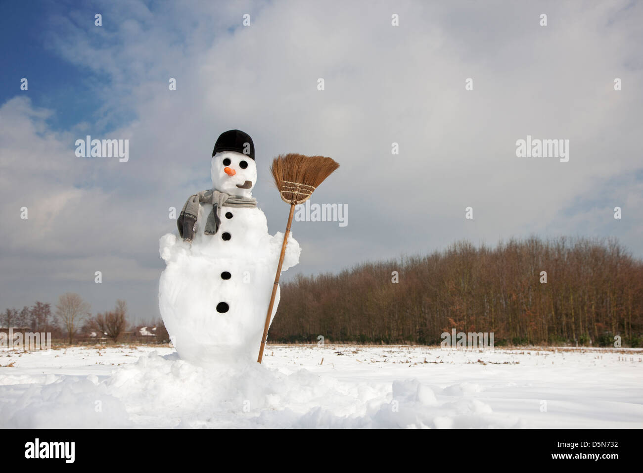 Decorated happy snowman with carrot nose, hat, pipe, scarf and broom in the snow in winter Stock Photo