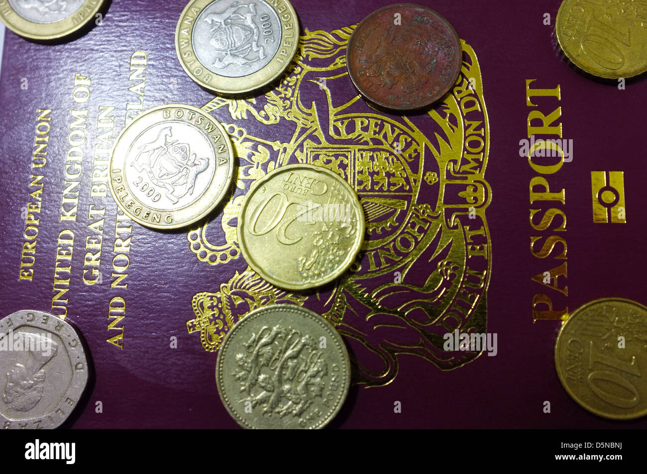 An image of the front page of a British passport covered in coins from the UK and Europe. Stock Photo