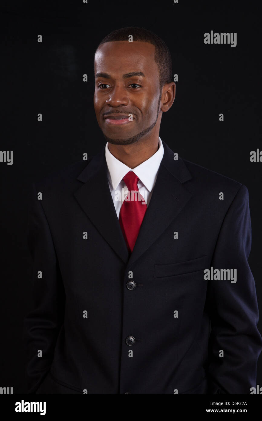 Black man in dark suit, white shirt and red tie, a successful, prosperous businessman, looking thoughtful but happy Stock Photo