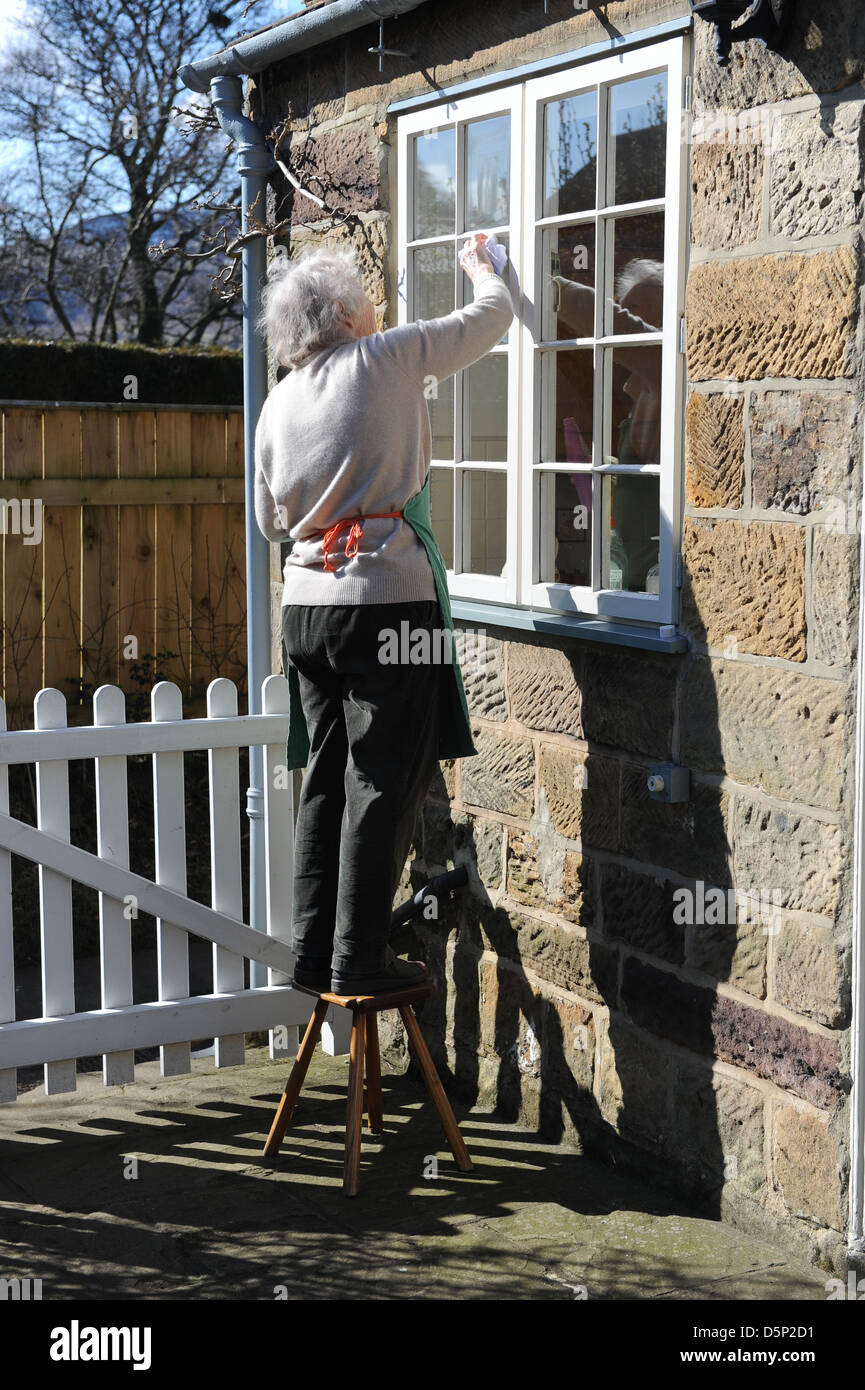 Female pensioner cleaning the windows of her home in North Yorkshire ...