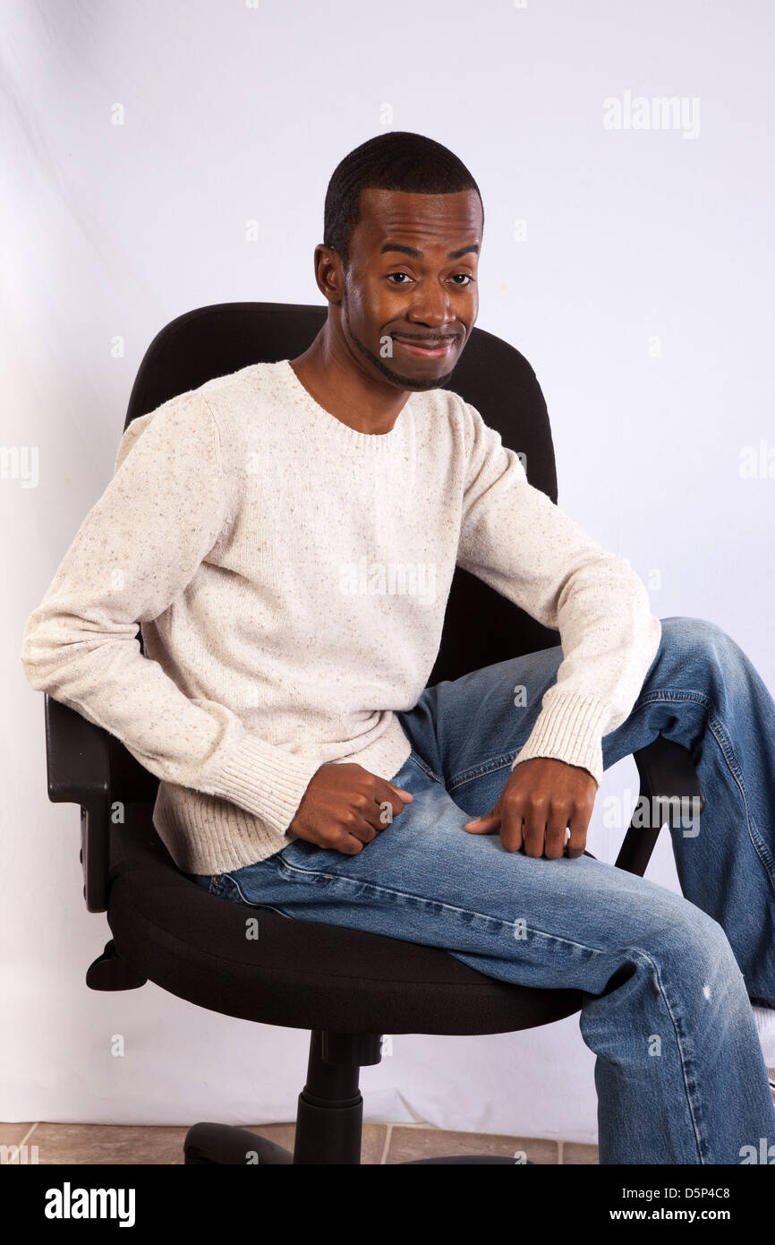 Handsome black man  in pullover shirt and blue jeans, sitting casually in a business chair, smiling at the camera Stock Photo