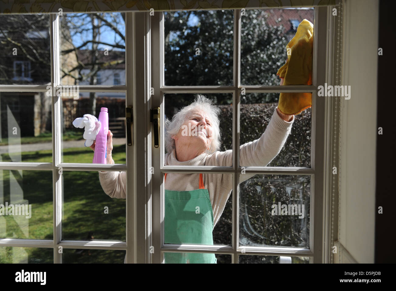 Elderly pensioner cleaning windows of her home in the sunshine Stock