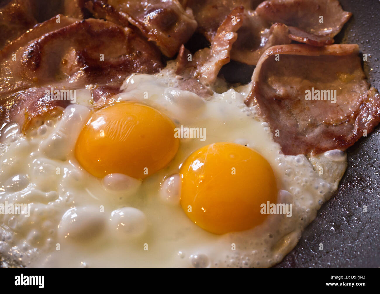 Double yolked egg and bacon frying for breakfast Stock Photo