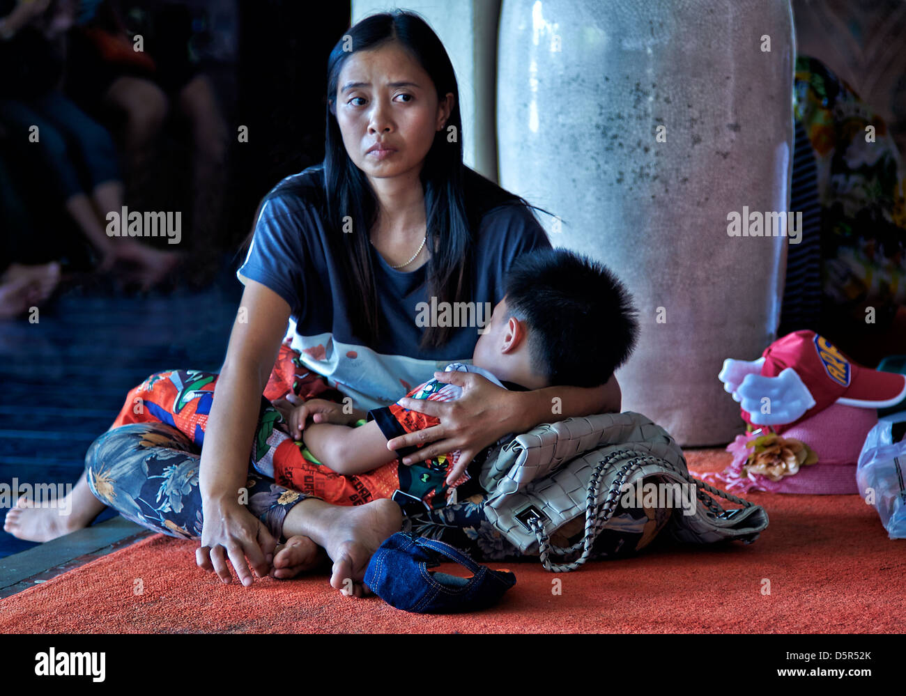Worried mother. Concerned and anxious Thai mother cradles her child whilst awaiting a doctors consultation. Thailand South East Asia Stock Photo
