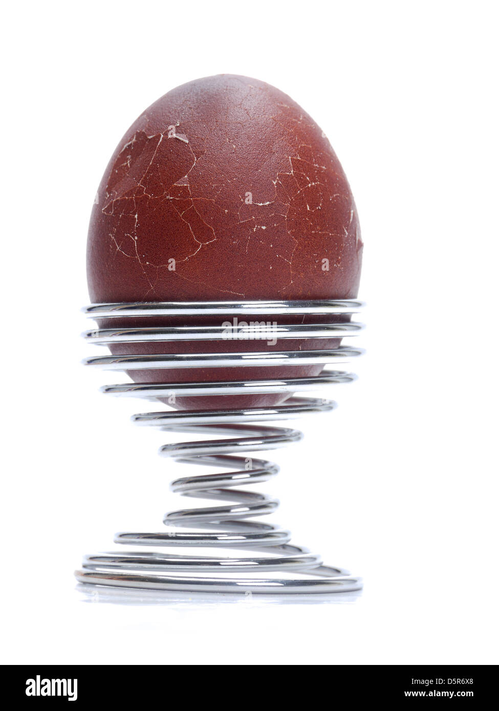 Dark brown soft-boiled egg with broken up egg shell in a spiral stand on white background Stock Photo
