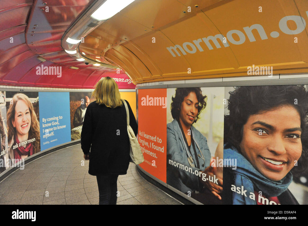 Oxford Circus station, London, UK. 8th April 2013. Commuters and tourists pass by the posters in the underground for the Mormon Church. The Church of Jesus Christ of Latter-day Saints launches an advertising campaign in London with the slogans "I'm a Mormon" and "Ask a Mormon", the campaign in tube stations and on buses is on the back of the stage comedy musical, The Book of Mormon. Stock Photo