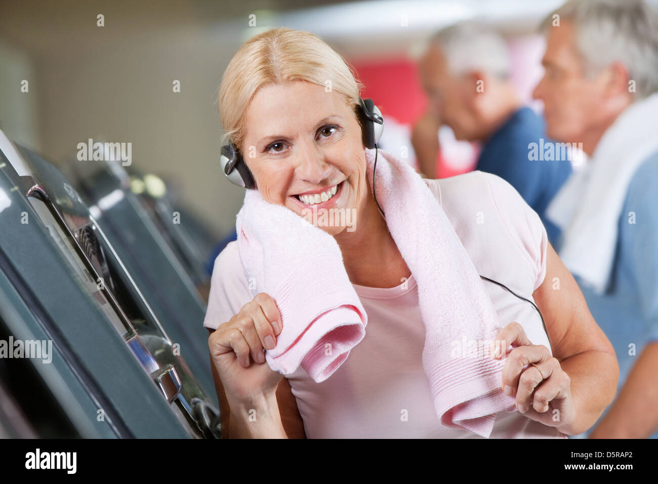 Happy active senior woman with headphones in fitness center Stock Photo