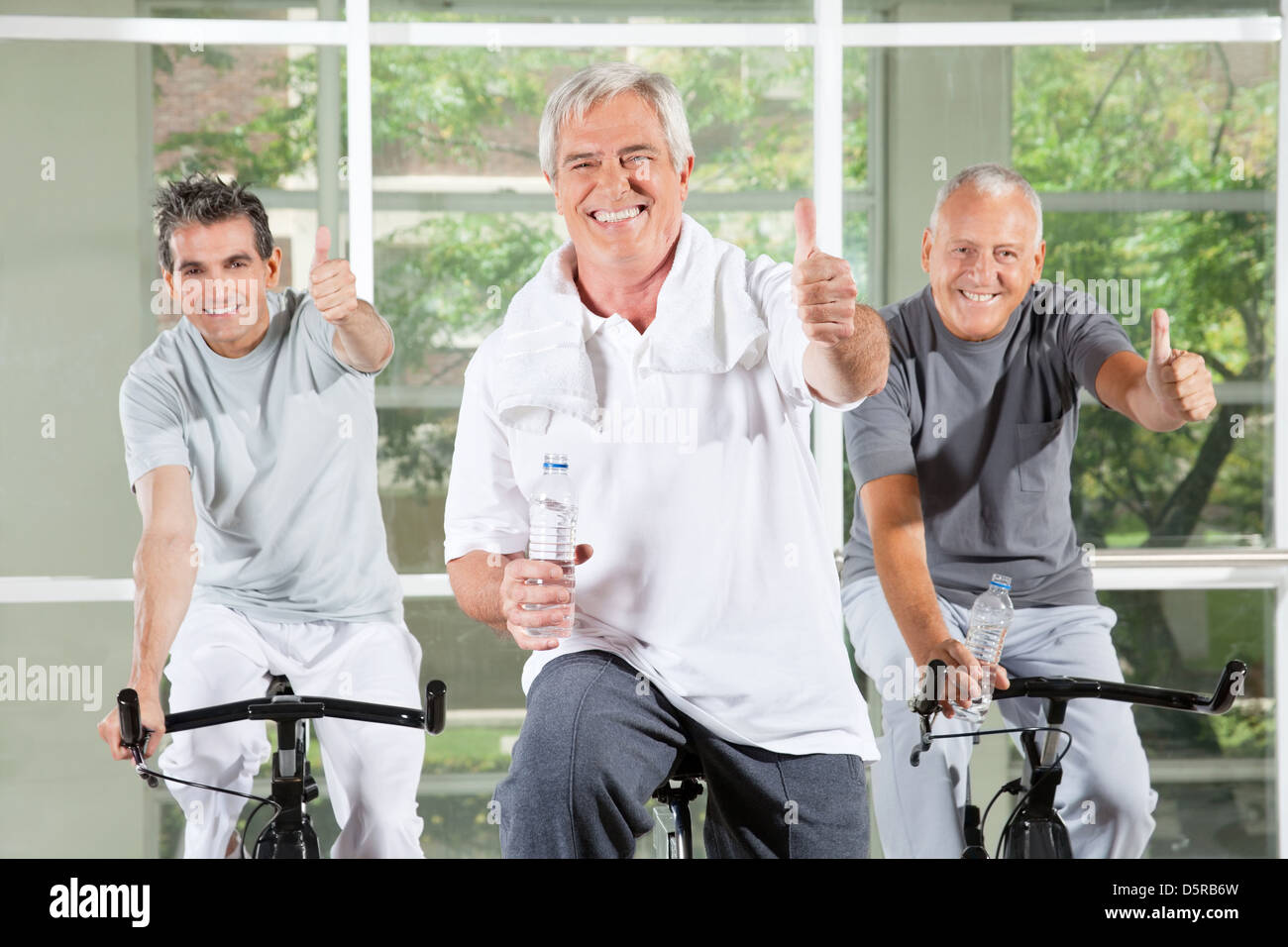 Three successful seniors holding thumbs up on bikes in gym Stock Photo ...