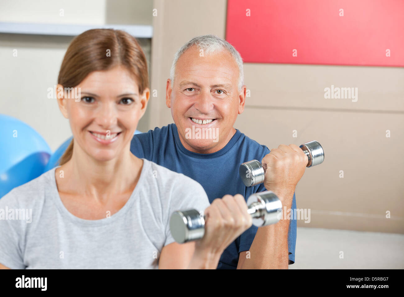 Two seniors lifting weights with dumbbells in fitness center Stock