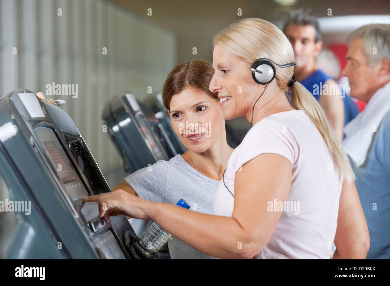 Senior woman with headphones running on treadmill in gym Stock Photo