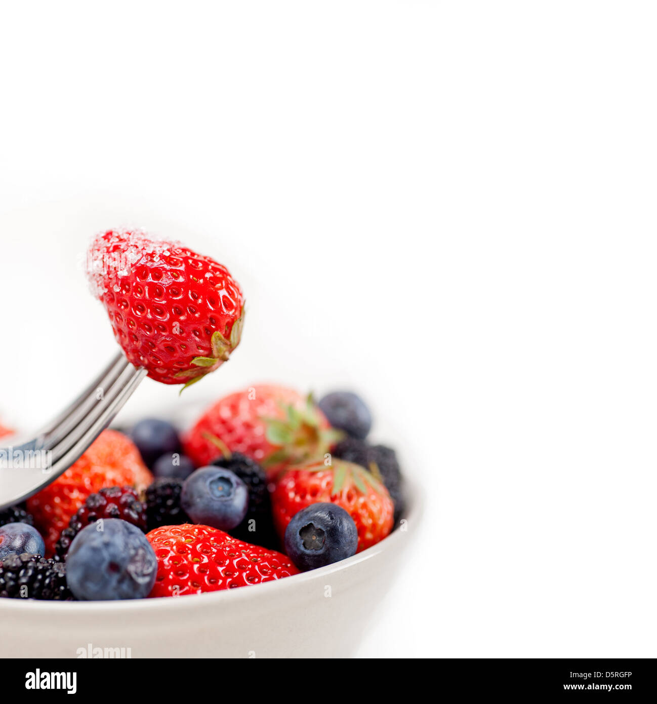 srawberry on a fork with sugar crust and bowl of mixed berries on white background Stock Photo