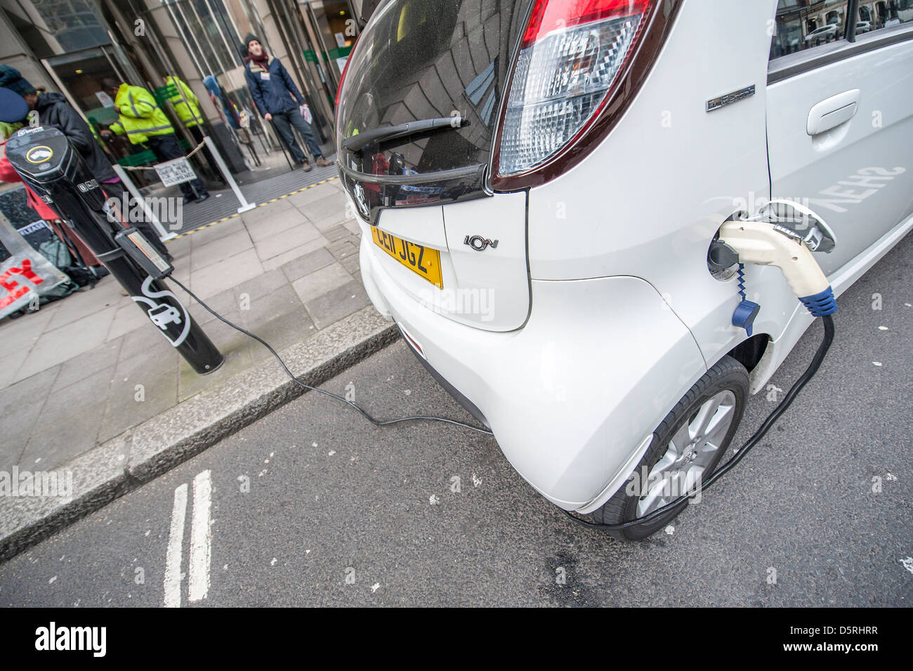 An electric car is charged outside the Department for Transport.  An anti road protest goes on in the background. Stock Photo