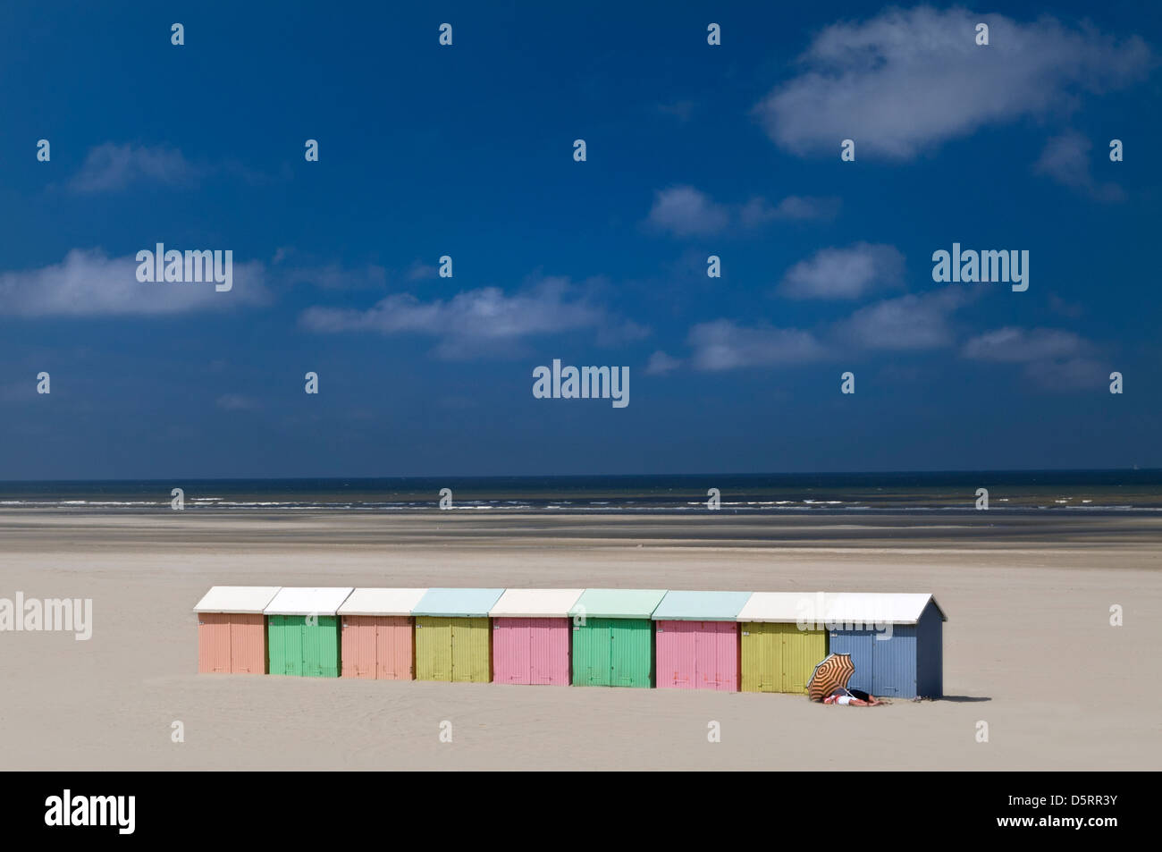 SEASCAPE Beach huts sand sun parasol Northern France coloured beach huts sun umbrella and sunbathing couple on beach Berck sur Mer France Stock Photo