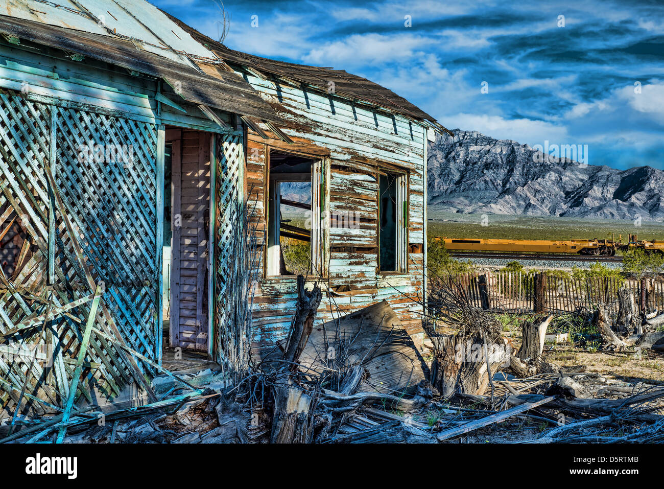 Abandoned cabin with beautiful dramatic sky and mountains in the background along with a brown picket fence, and train tracks Stock Photo