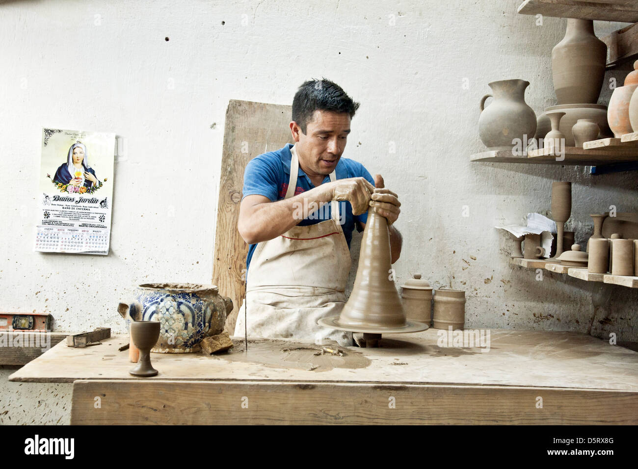 skilled potter craftsman turns Talavera clay on potters wheel as finished pieces cure on nearby shelves Uriarte factory Puebla Stock Photo