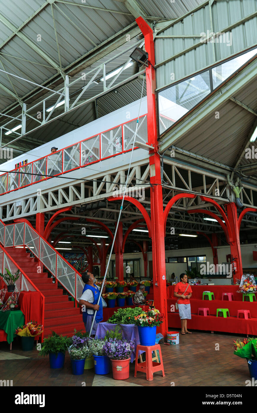 A workman using a paint roller on a long pole inside the public market