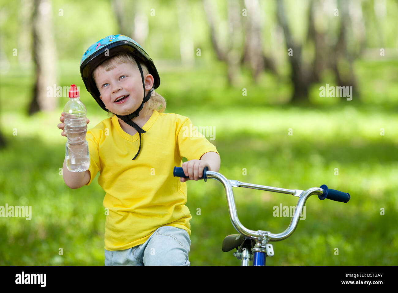 Cute kid on bicycle. Child holding bottle with water. Stock Photo