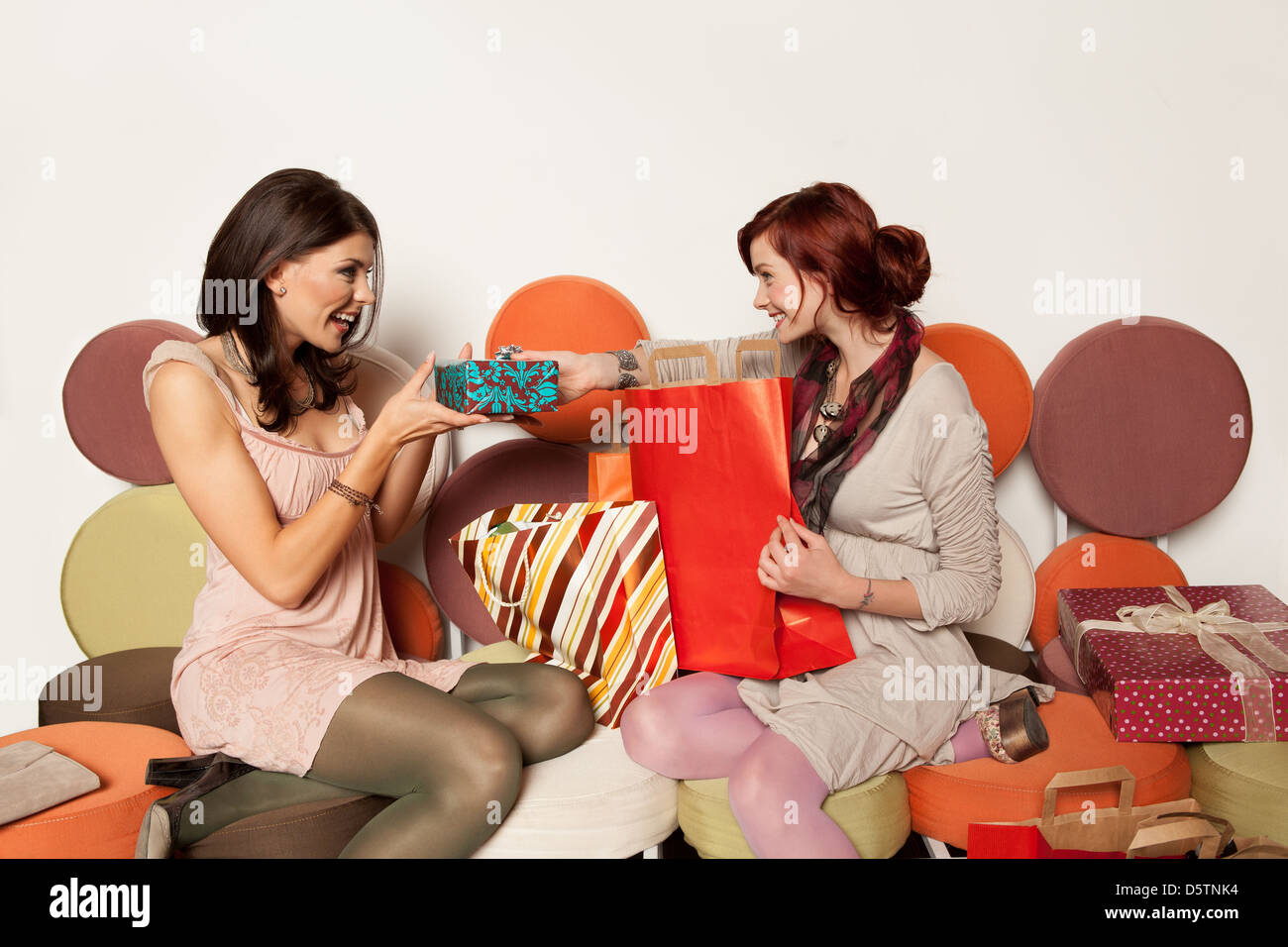 young girls exchanging gifts on a colorful sofa Stock Photo