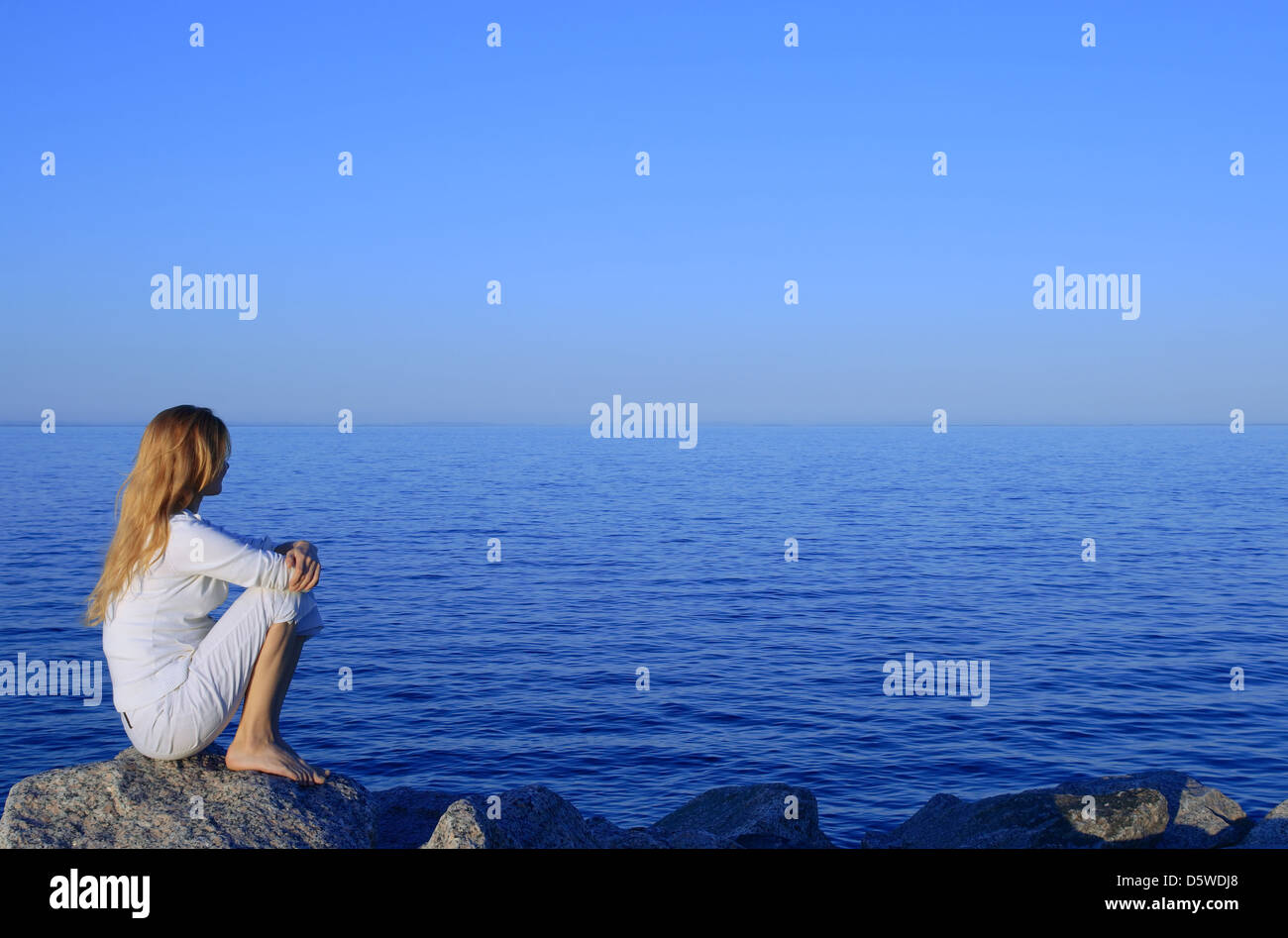 Girl sitting on the rock by the peaceful sea at sunset Stock Photo - Alamy