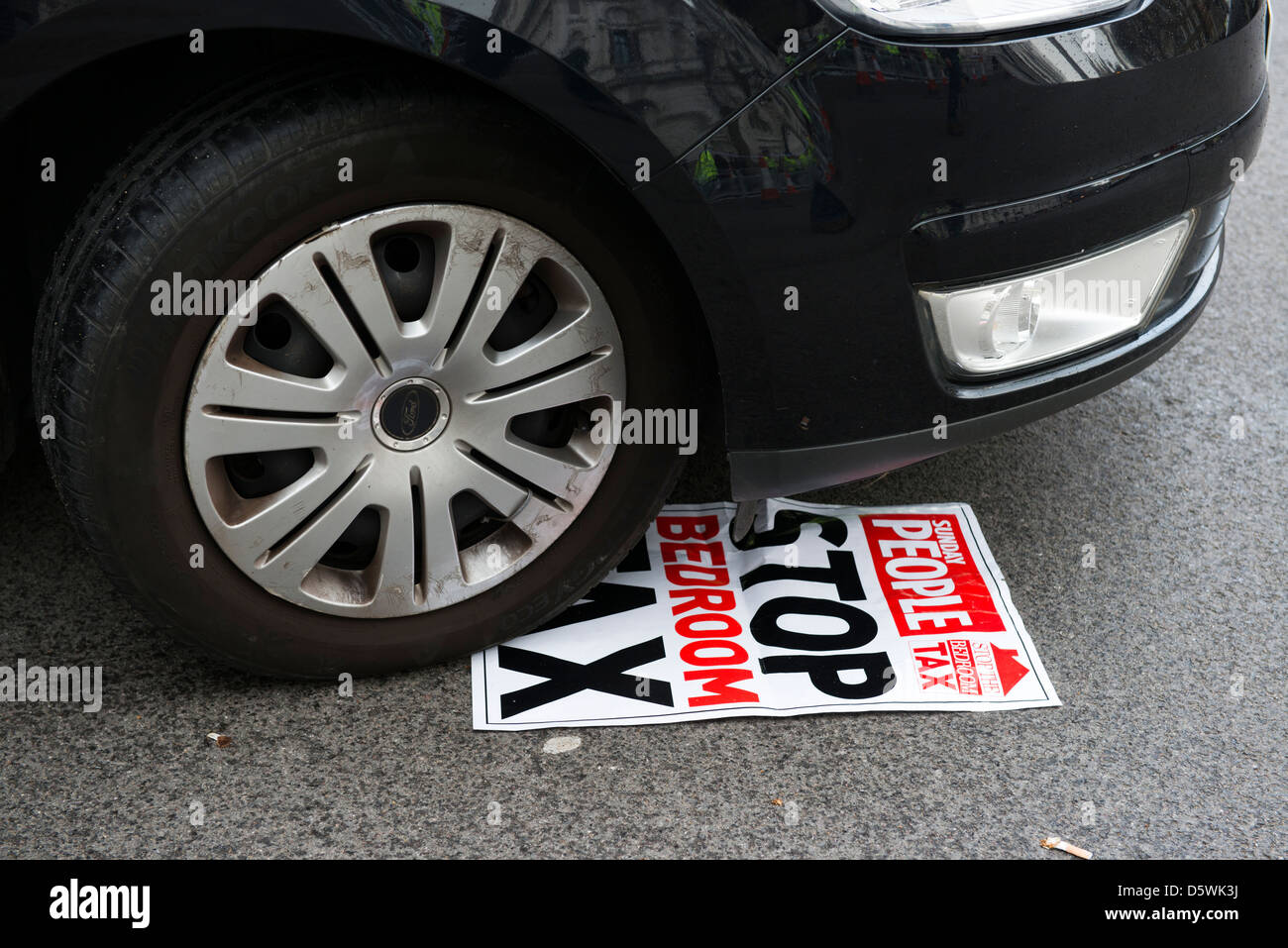 A car drives over a discarded poster for 'Stop the Bedroom Tax' in Westminster, London on 30th March 2013 Stock Photo