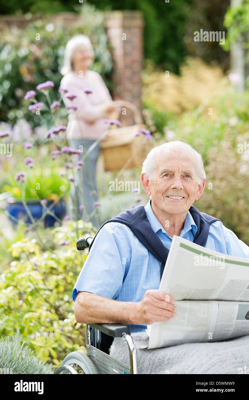 Older man in wheelchair reading newspaper outdoors Stock Photo