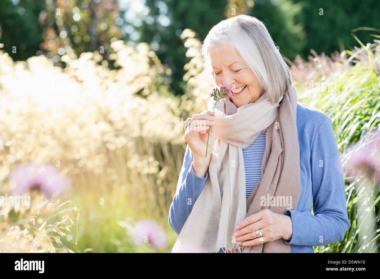 Older woman smelling flowers outdoors Stock Photo