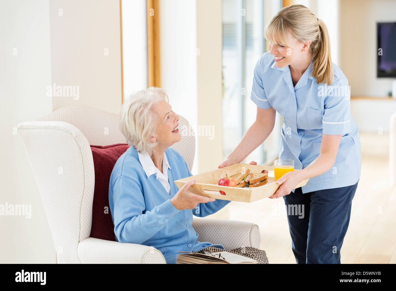 Caregiver giving older woman tray of food Stock Photo